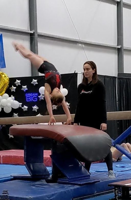 Gymnast performing vault with coach observing in a gym.
