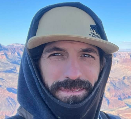 Man in hoodie and Grand Canyon hat smiles at the Grand Canyon.