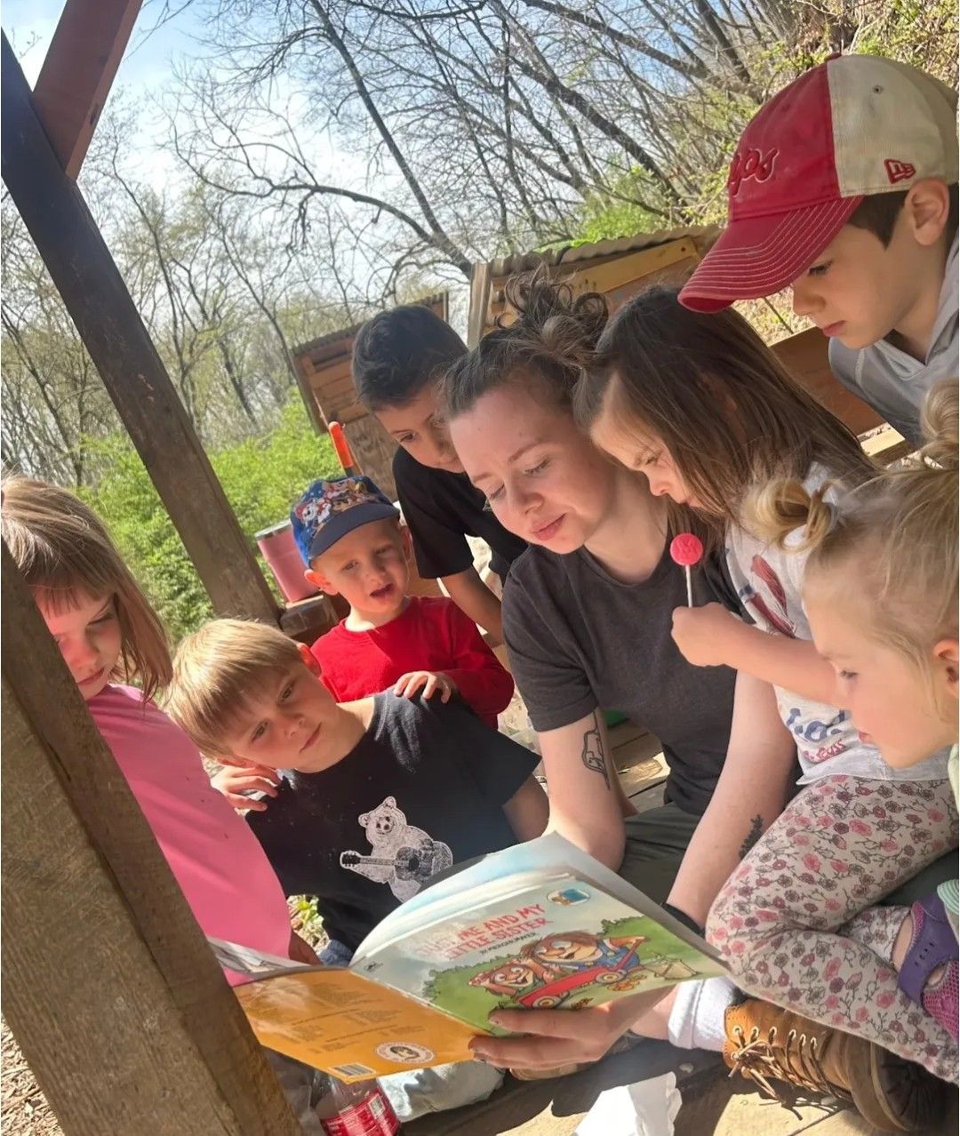 Group of children and adult reading a book outdoors.