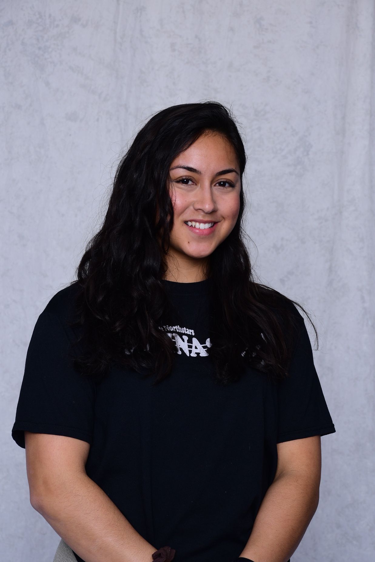 Smiling woman with dark hair wearing a black t-shirt. Posed against a mottled gray backdrop.