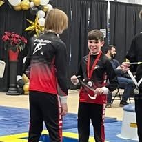 Two kids in athletic gear with medals, smiling. One child is holding a medal.