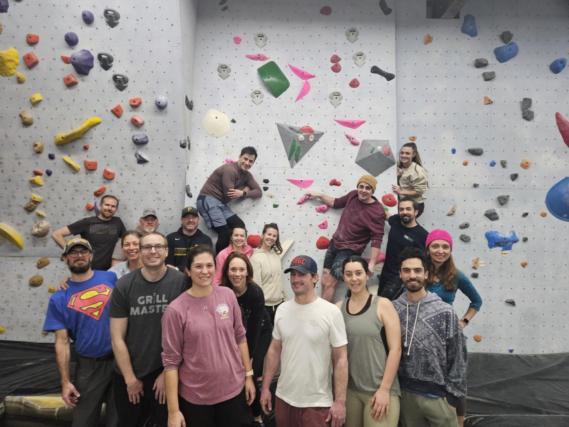 Group of people posing in front of a colorful rock climbing wall; some are climbing, smiling.