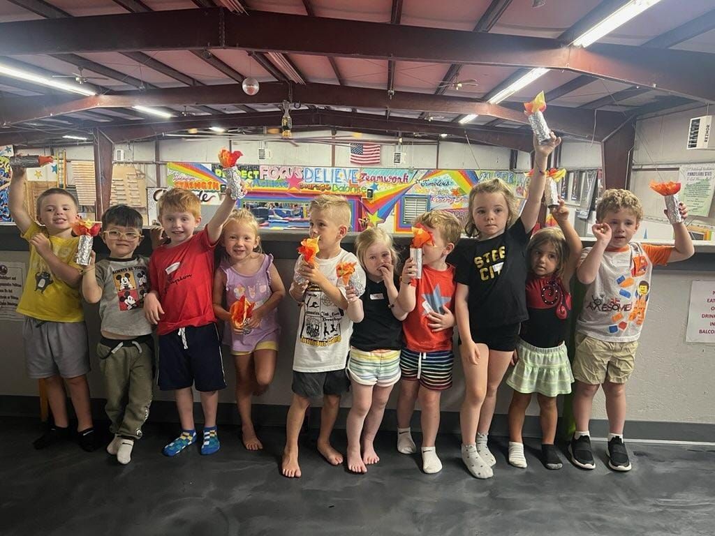 Group of kids holding up orange toys in an indoor setting, smiling for the camera.