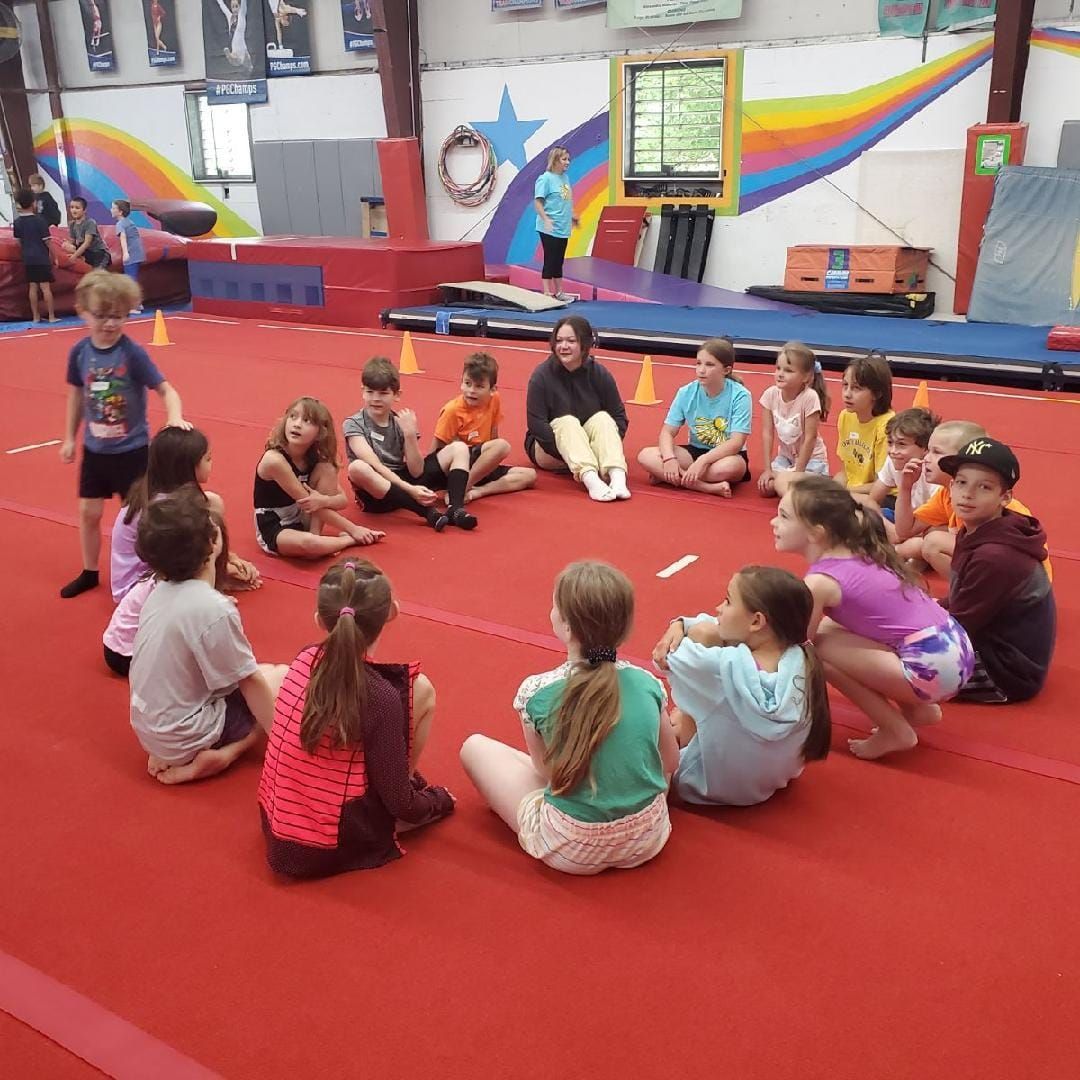Children and instructor in a circle on a red mat in a gymnastics studio.