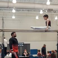 Gymnast on parallel bars, coach watching. Indoor gym.