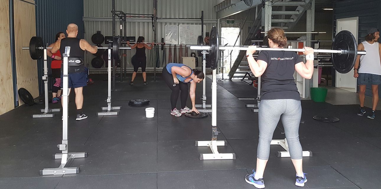 A group of people are squatting with barbells at Marky Marks Personal Training & Gym in Moss Vale