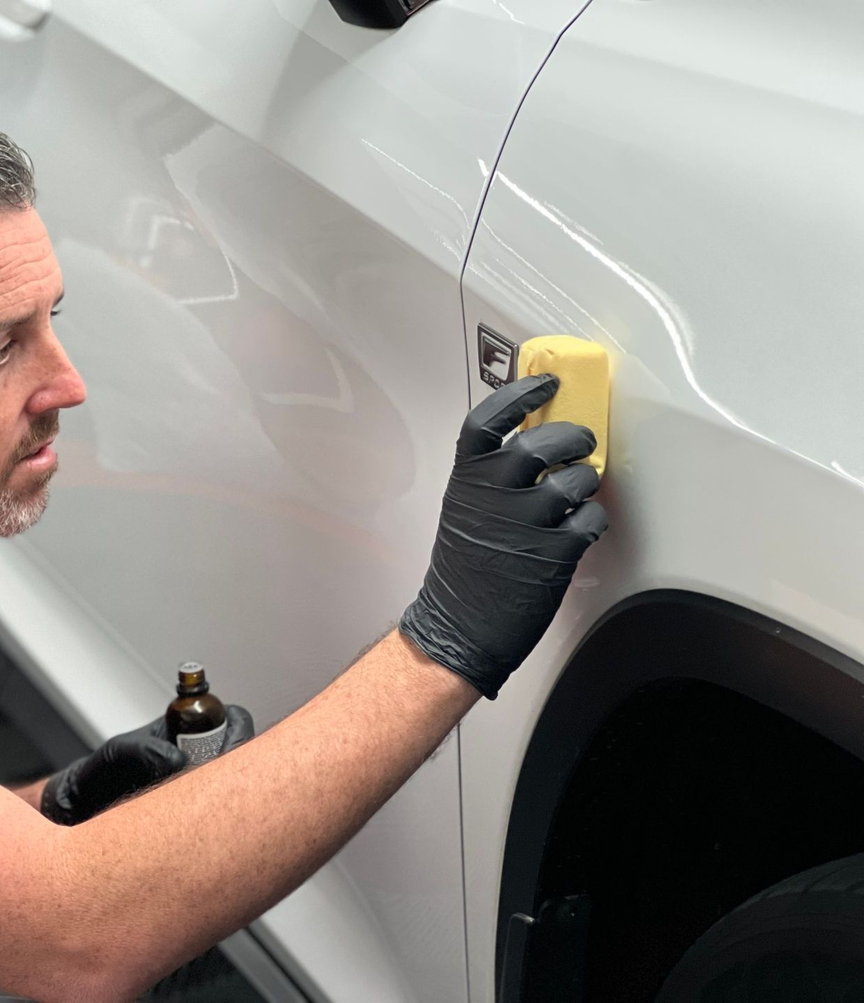 A person wearing black gloves is polishing the hood of a red car.