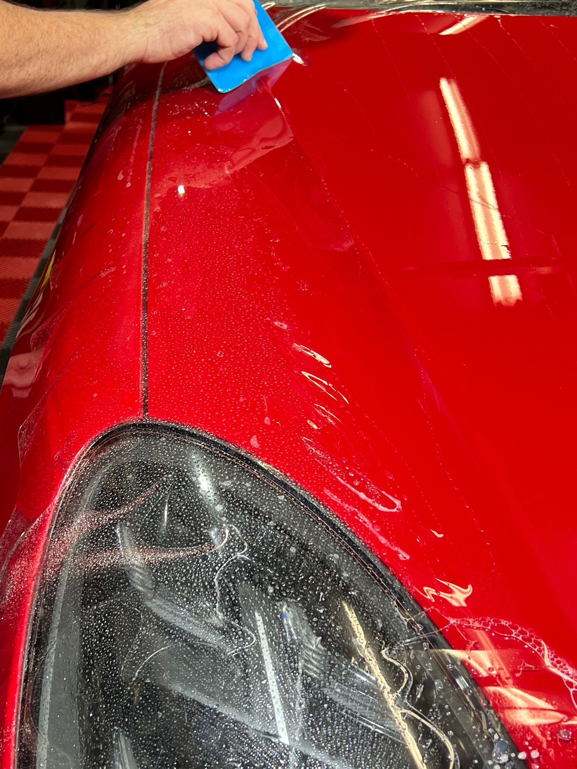 A person is cleaning a red car with a blue sponge