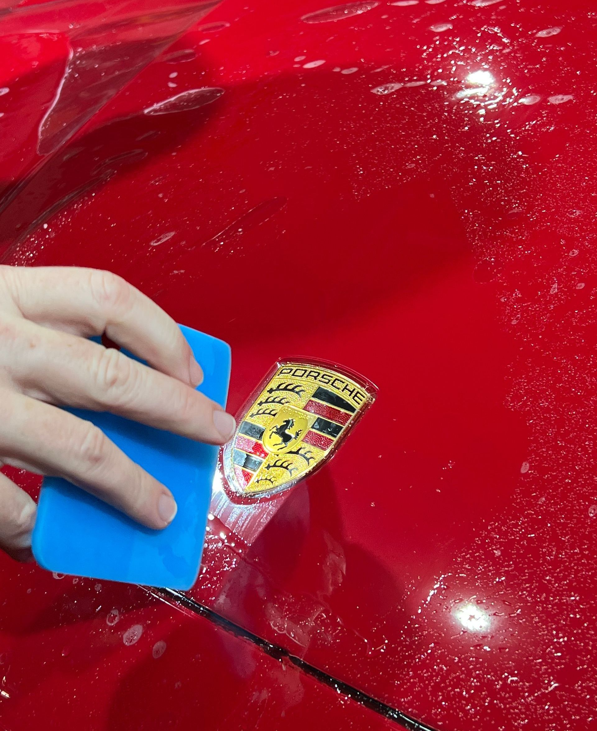 A person wearing black gloves is polishing the hood of a red car.