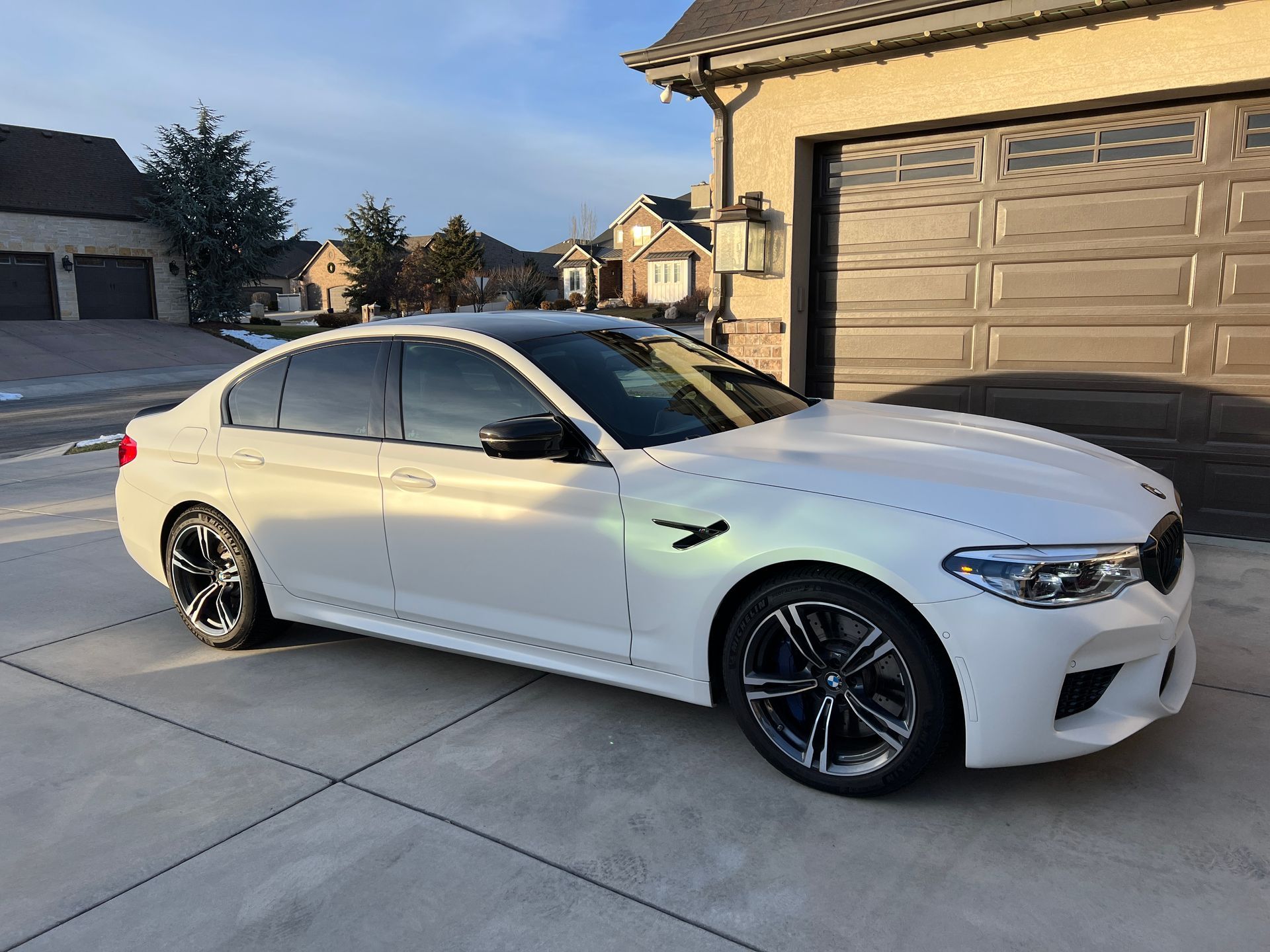 A white bmw m5 is parked in front of a garage door.