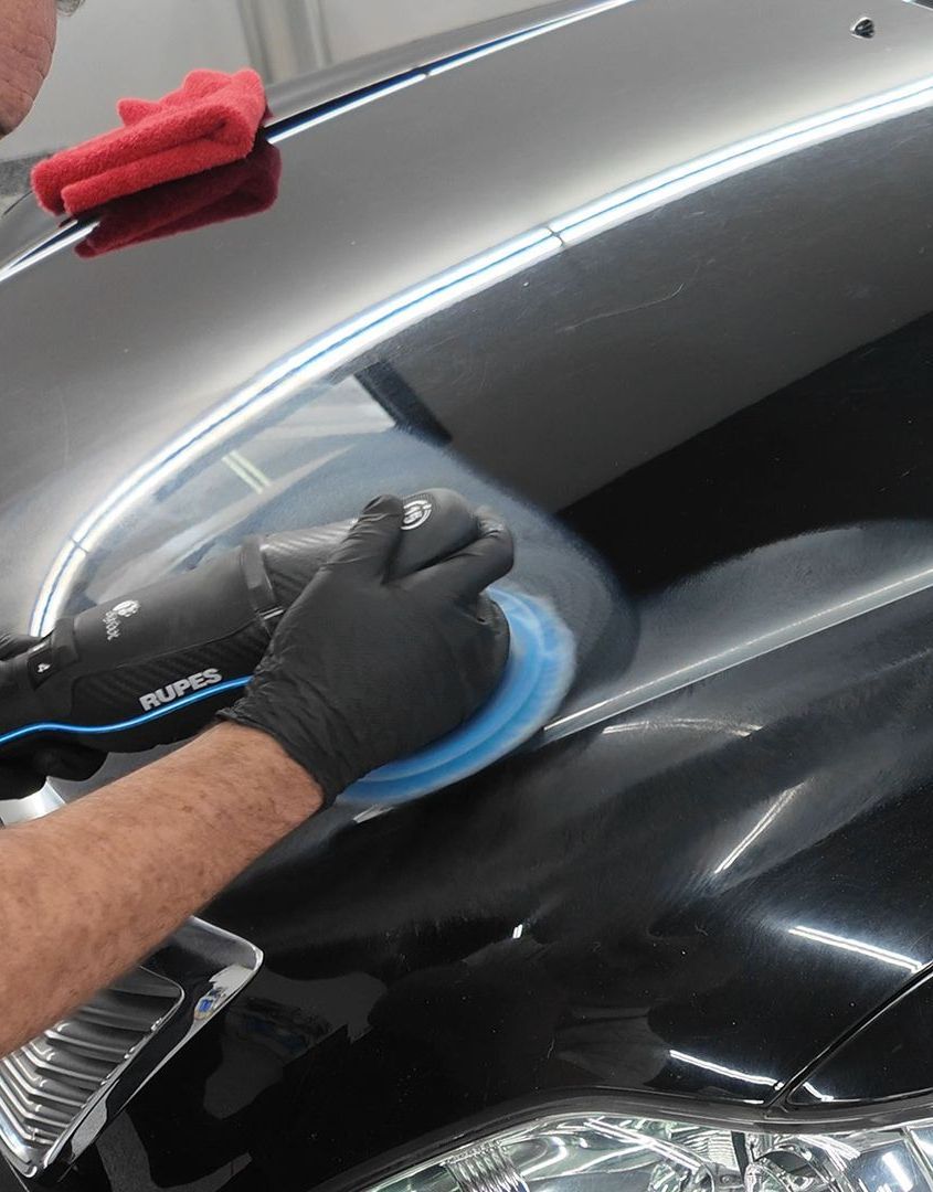 A person wearing black gloves is polishing a black car