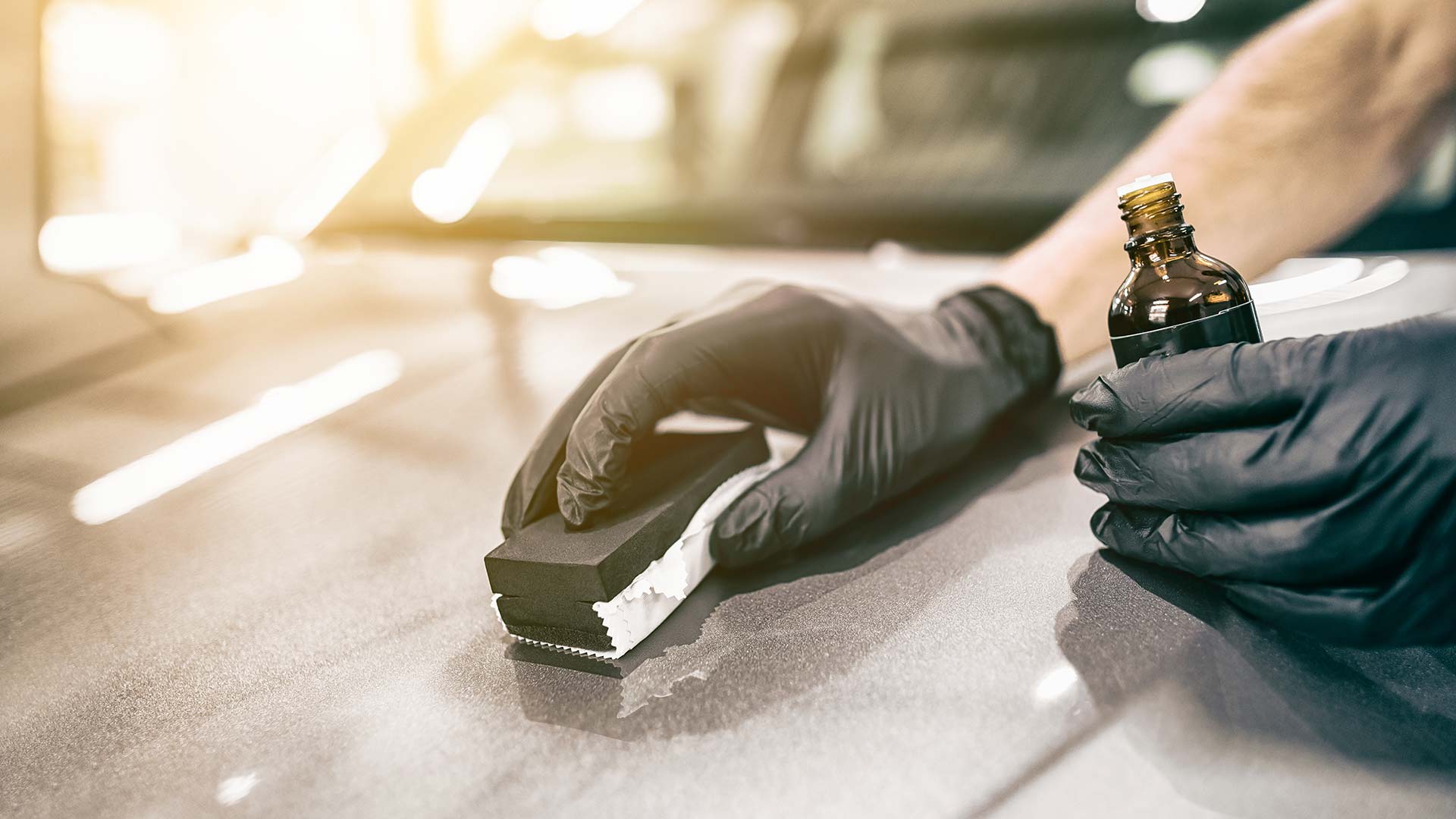 A person wearing black gloves is polishing a car with a sponge.