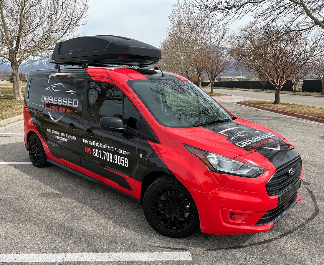 A red and black van with a roof rack is parked in a parking lot.