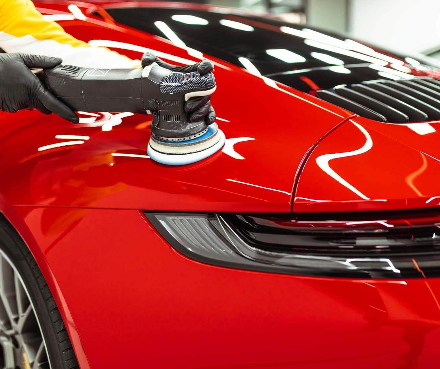 A person is polishing a red car with a machine.