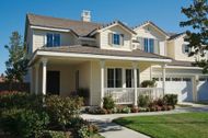 Two-story cream suburban house with a front porch, garage, and neatly landscaped lawn