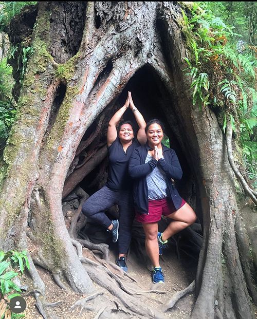 Two women doing yoga inside a tree, arms raised in a forest.