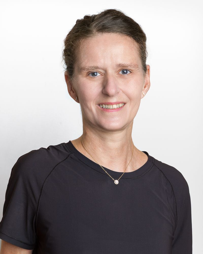 Woman with curly brown hair smiles at the camera against a gray backdrop.