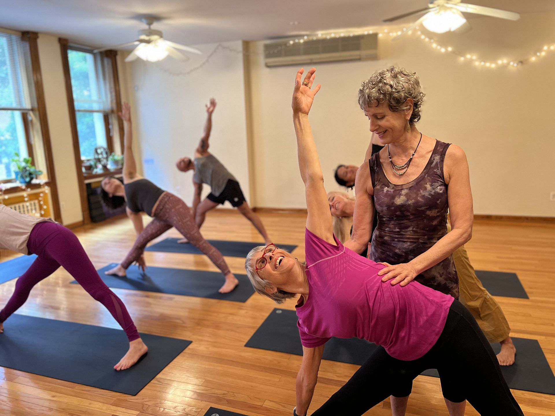 Woman in a yoga pose, sitting with one leg extended and reaching for her foot; black shorts, white top.