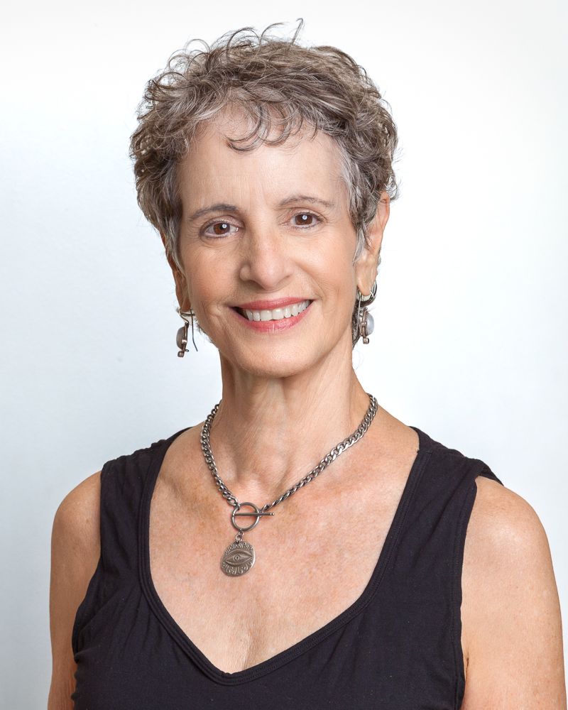 Woman with short gray hair, smiling, wearing earrings, patterned scarf, and red top.