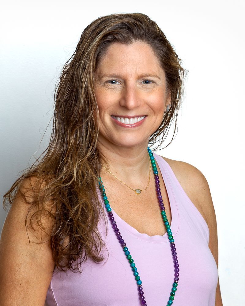 Woman with light skin smiling, wearing pink scarf and colorful blouse.