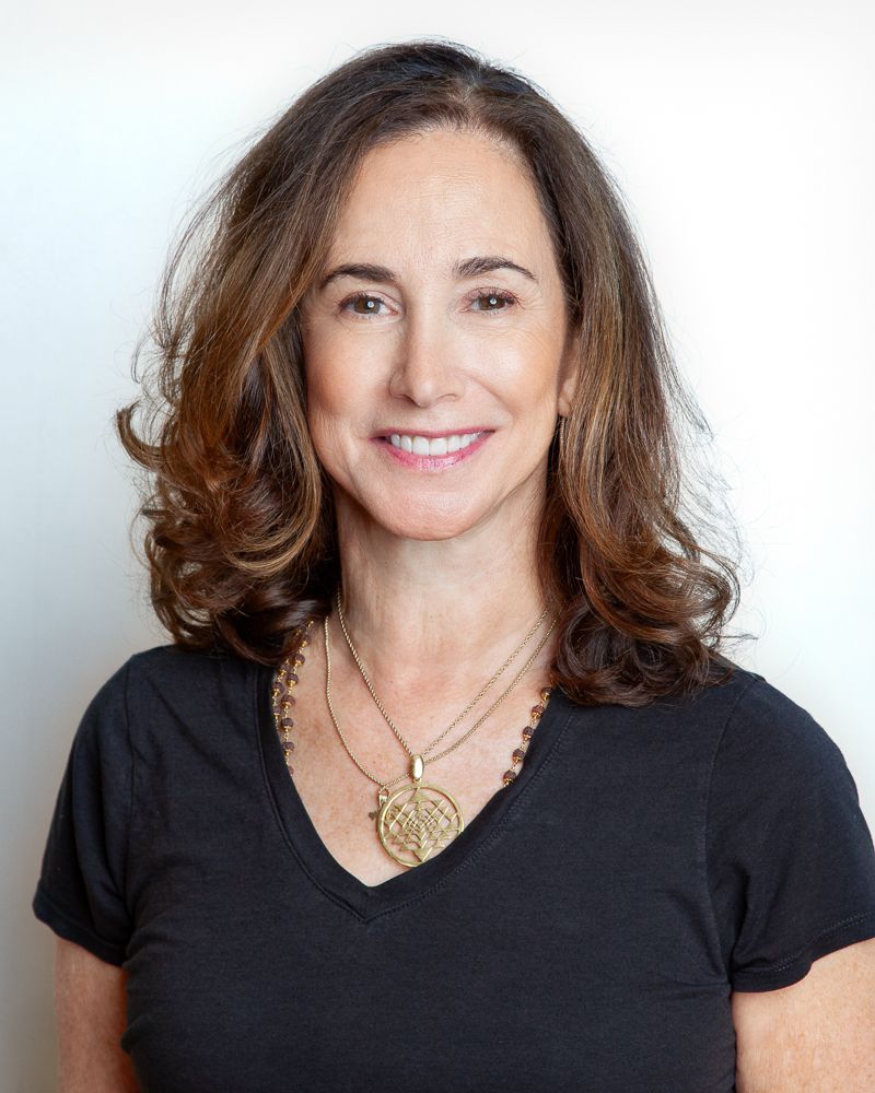 Woman with blonde hair, wearing gold earrings, smiling slightly, indoors.