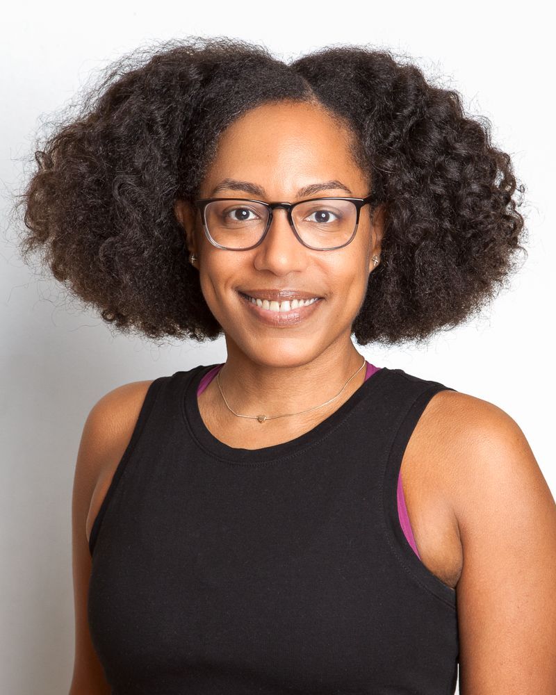 Person with afro, glasses, and floral shirt smiling. Inside vehicle.