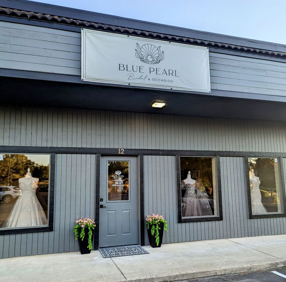 Blue Pearl boutique exterior with a gray door and windows displaying wedding dresses; planters flank the door.
