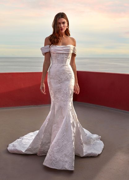Woman in white wedding dress with high slit, standing outdoors at sunset.