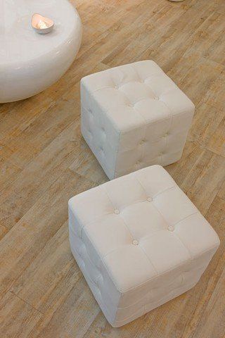 Zwei weiße Ottomanen stehen auf einem Holzboden neben einem weißen Couchtisch.