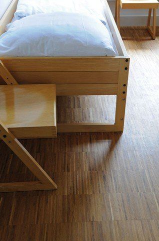 Neben einem Holzbett steht ein Holzstuhl.