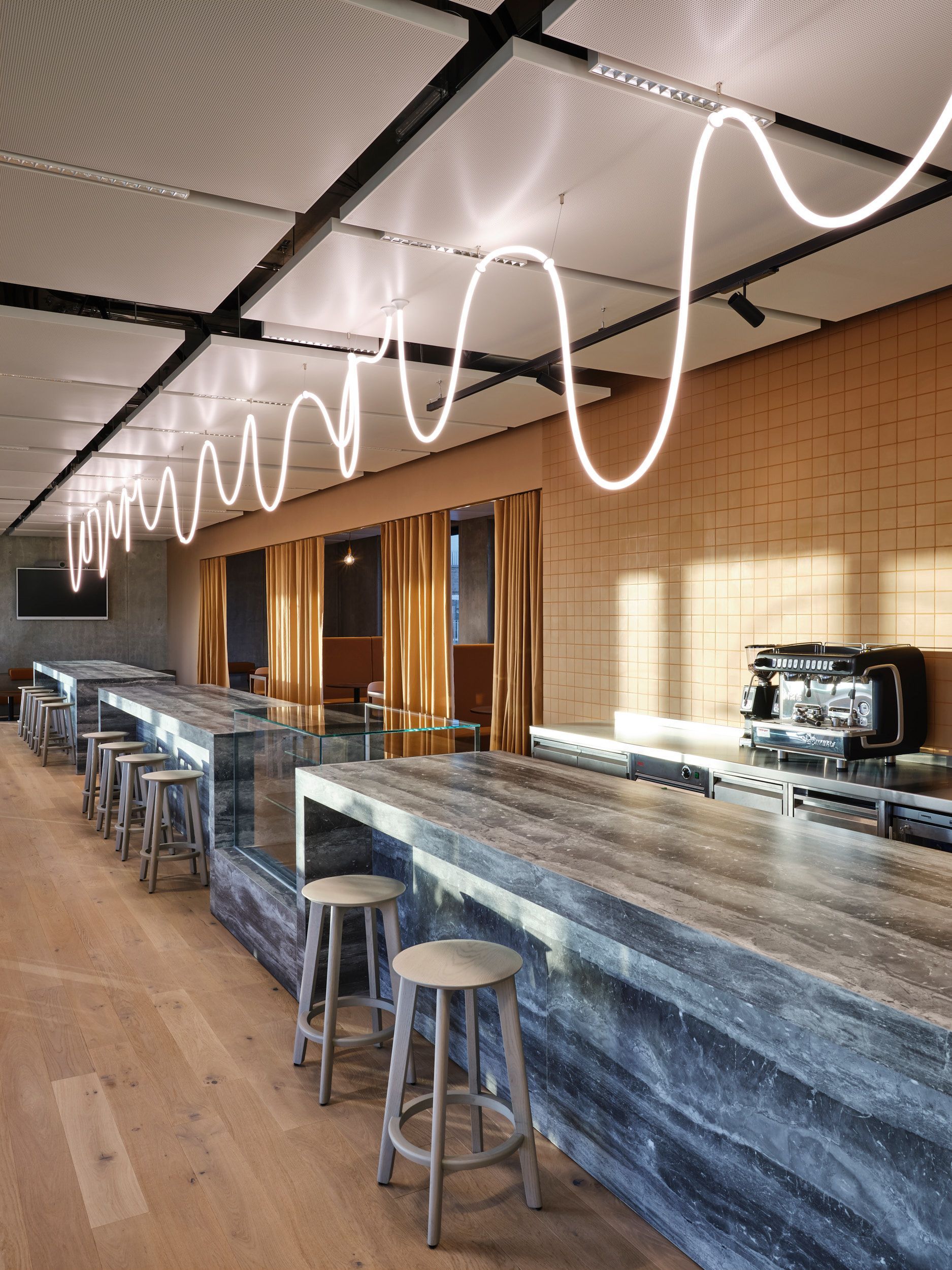 Ein langer Raum mit Tischen und Hockern und einer Neonlampe, die von der Decke hängt.