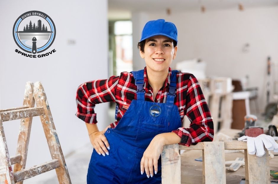 A drywall repair contractor wearing a blue cap, red plaid shirt, and blue overalls stands confidently inside a commercial renovation site. She leans on a wooden surface with a ladder and work gloves nearby, smiling warmly. The project is near Bridgeview Close, and Bridgeview Dr, Fort Saskatchewan, AB.