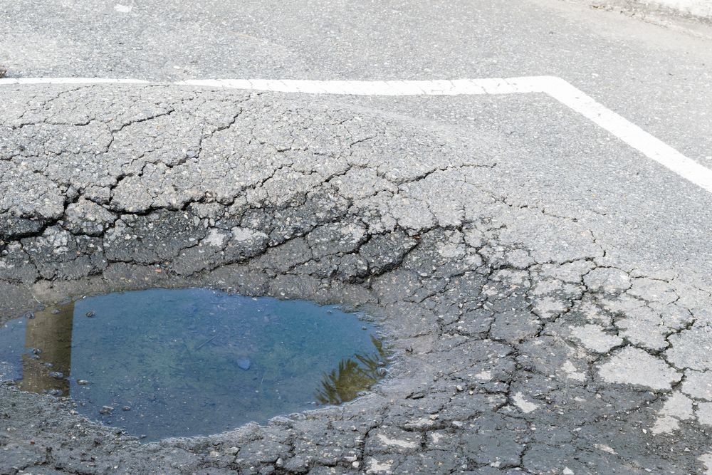 Cracked asphalt road with a large pothole filled with water