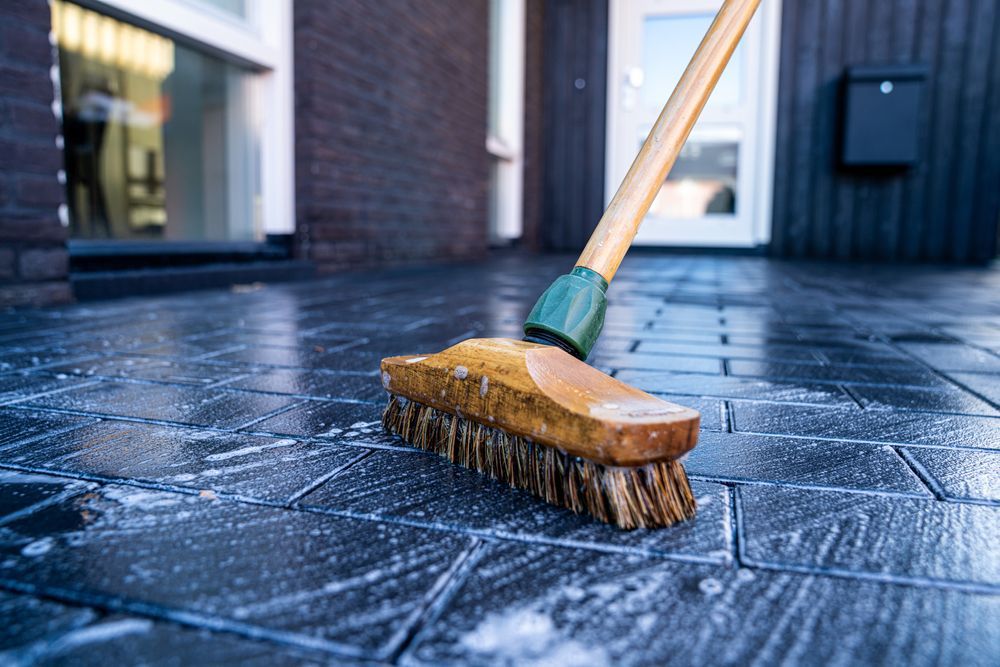 Cleaning a concrete patio with a broom and concrete-safe cleaner.