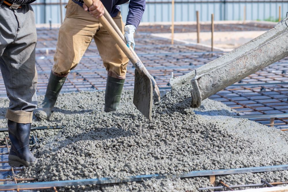 Workers pouring concrete onto a rebar foundation, using a shovel and hose.
