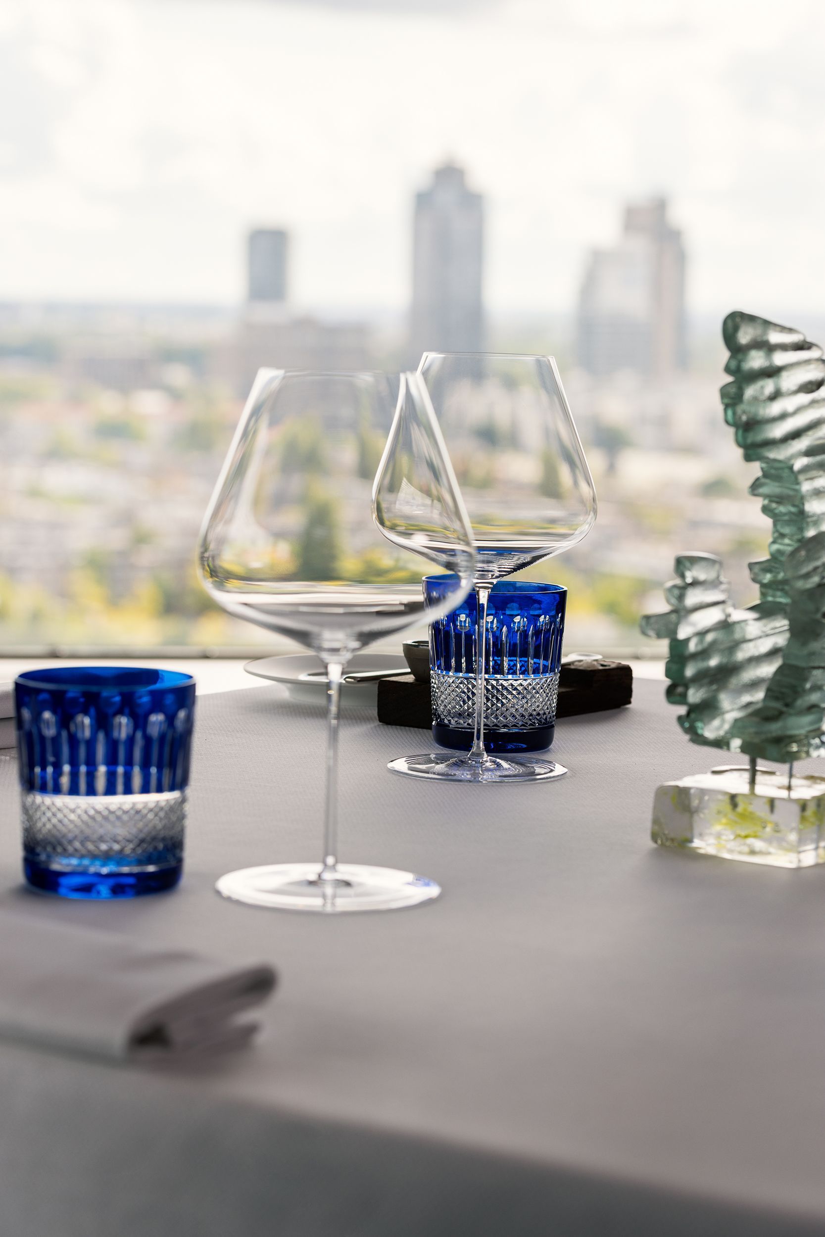 Table set with blue glasses and wine goblets overlooking a city skyline