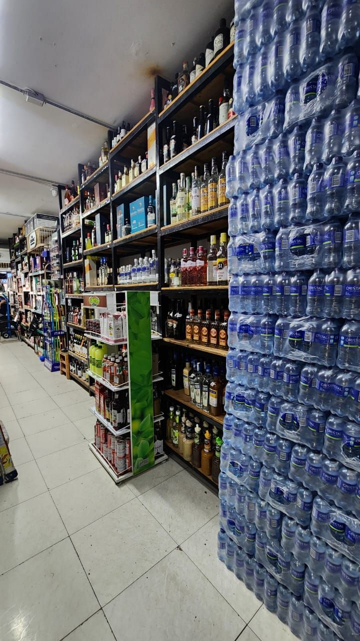 Pasillo de una tienda con estantes repletos de licor, otros alimentos y una gran pila de agua embotellada.