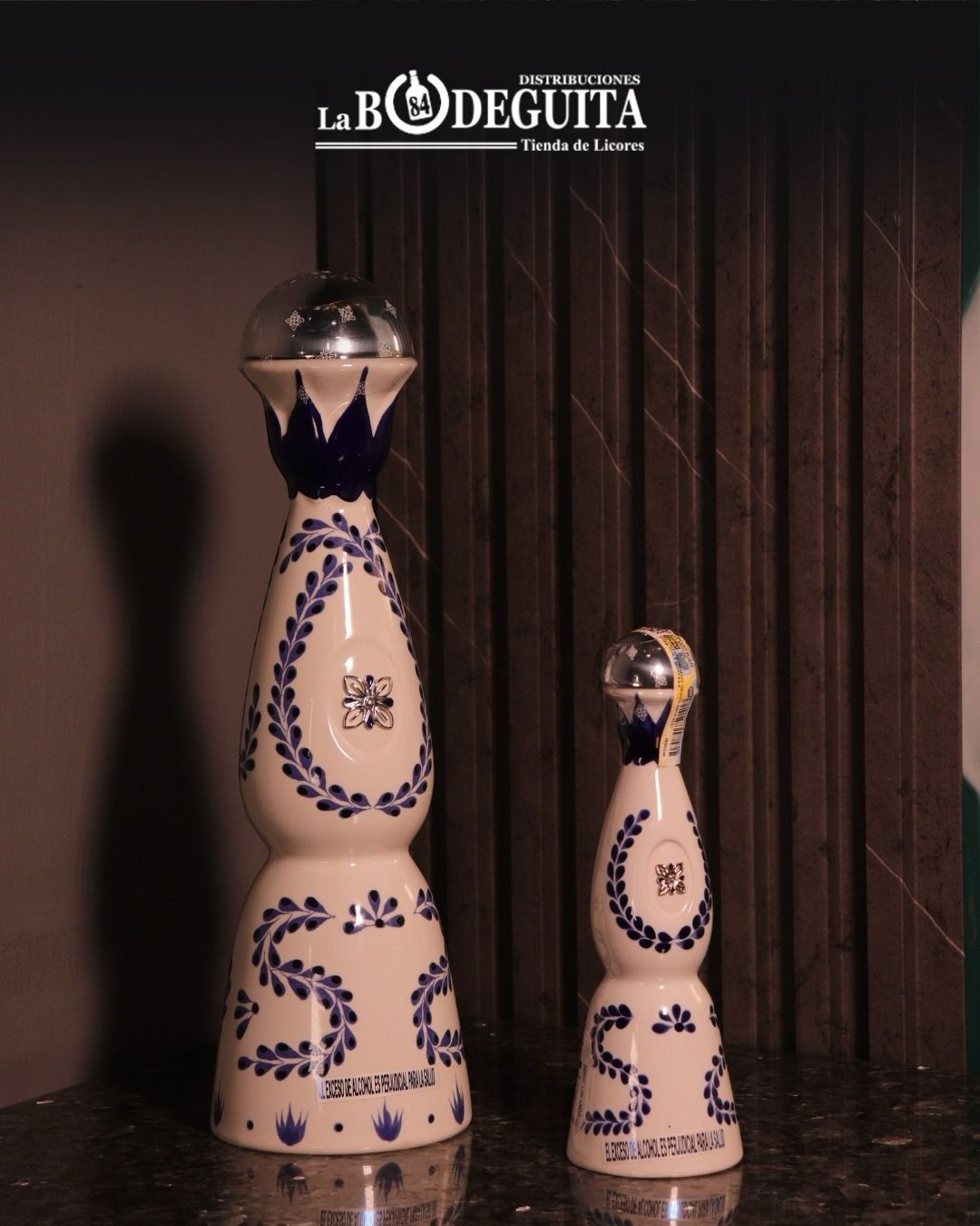 Dos botellas de tequila decorativas, blancas con diseños florales azules, sobre una encimera oscura.