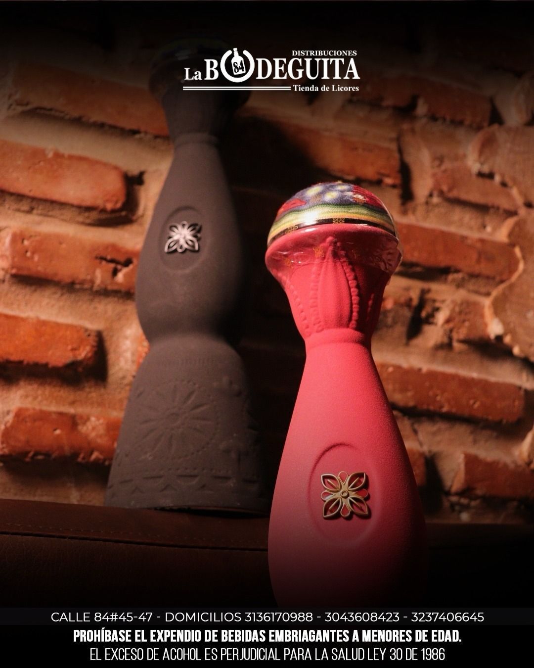 Dos botellas de tequila, una marrón y otra rosa, se encuentran en un estante contra una pared de ladrillos