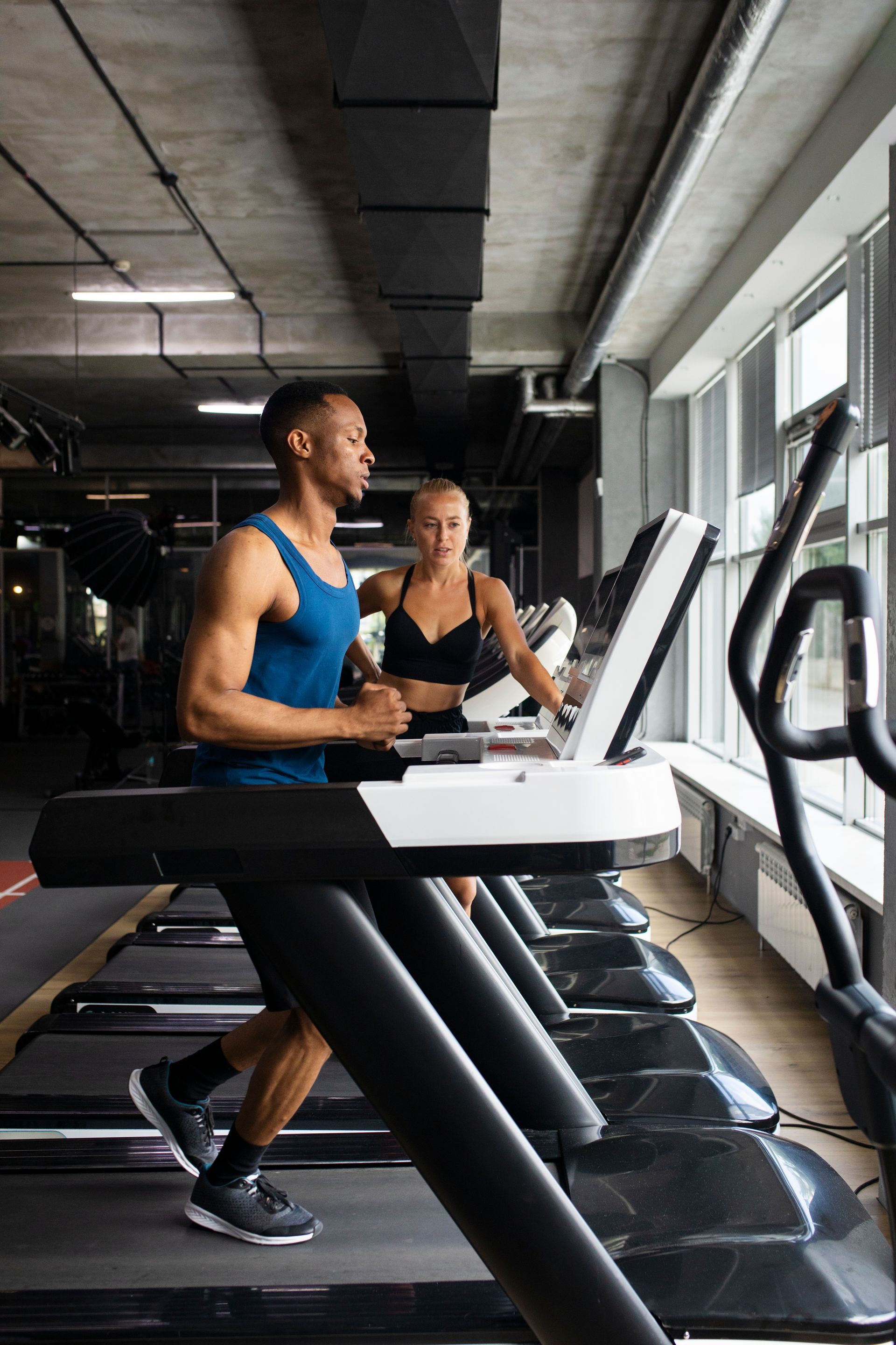 Un homme et une femme courent sur des tapis roulants dans une salle de sport.