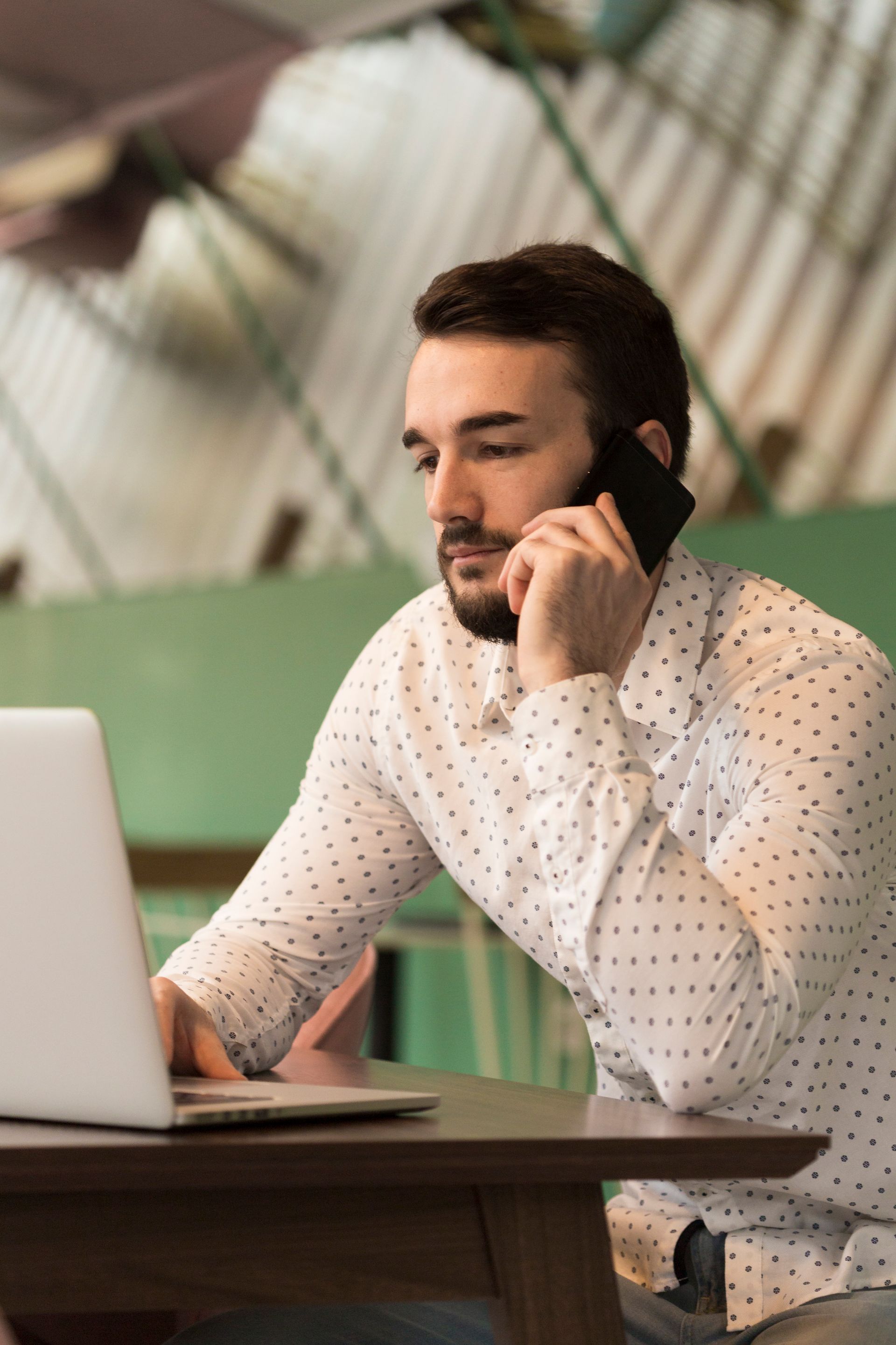 Un homme est assis à une table avec un ordinateur portable et parle sur un téléphone portable.
