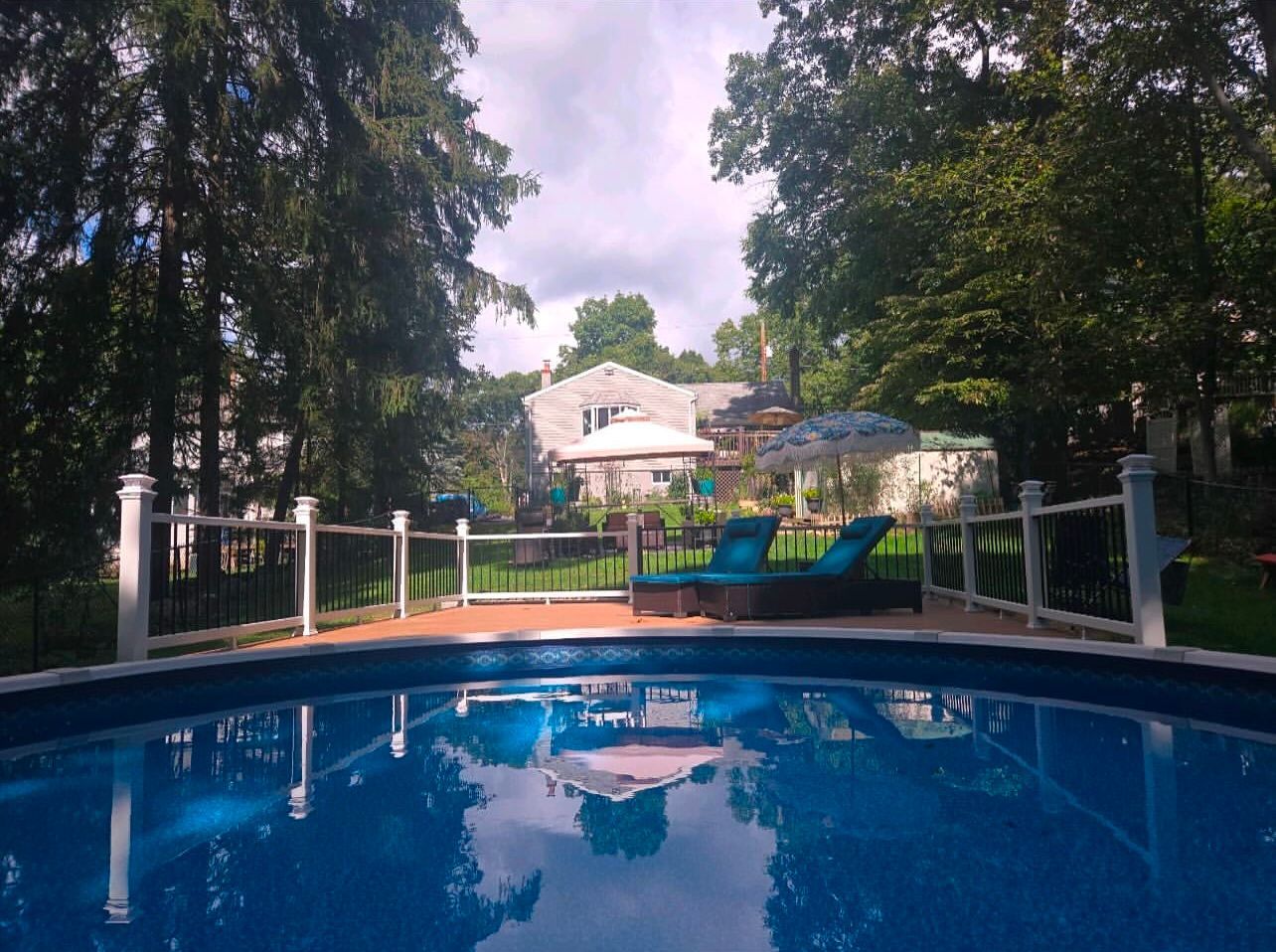 Backyard with a pool, lounge chairs, and a house in the background on a sunny day.