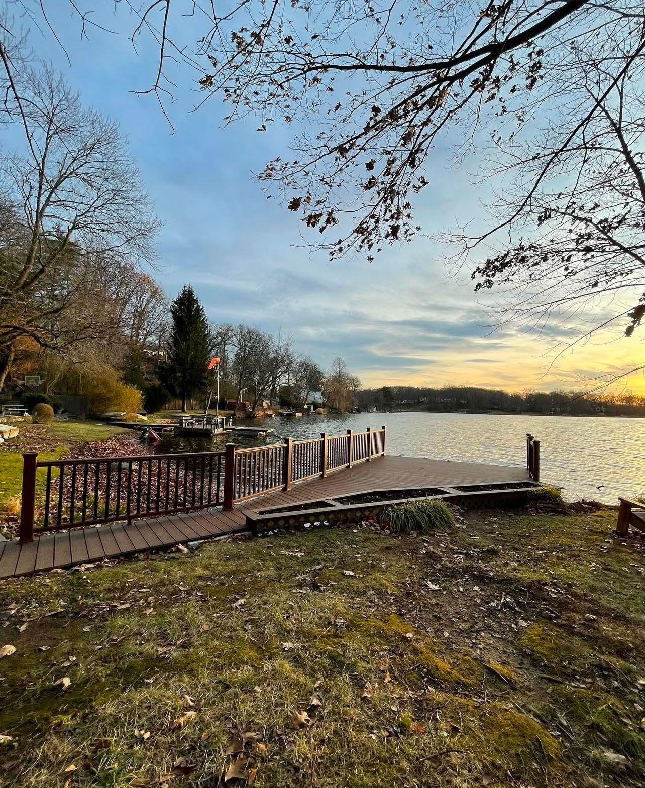 Wooden dock extending over calm water at dusk, surrounded by trees and grass.
