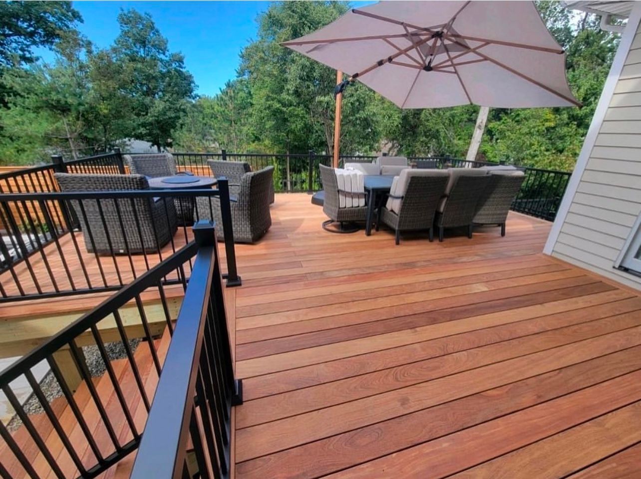 Wooden deck with patio furniture under an umbrella, surrounded by trees.