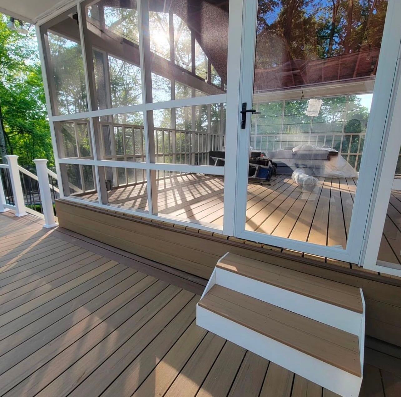 Wooden deck with steps, leading to a screened porch. Sunlight streams through the trees, illuminating the porch.