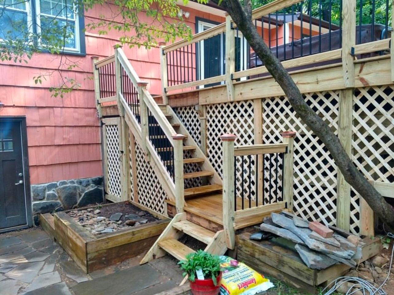 Wooden deck with stairs, lattice siding, and black railing on a pink building.