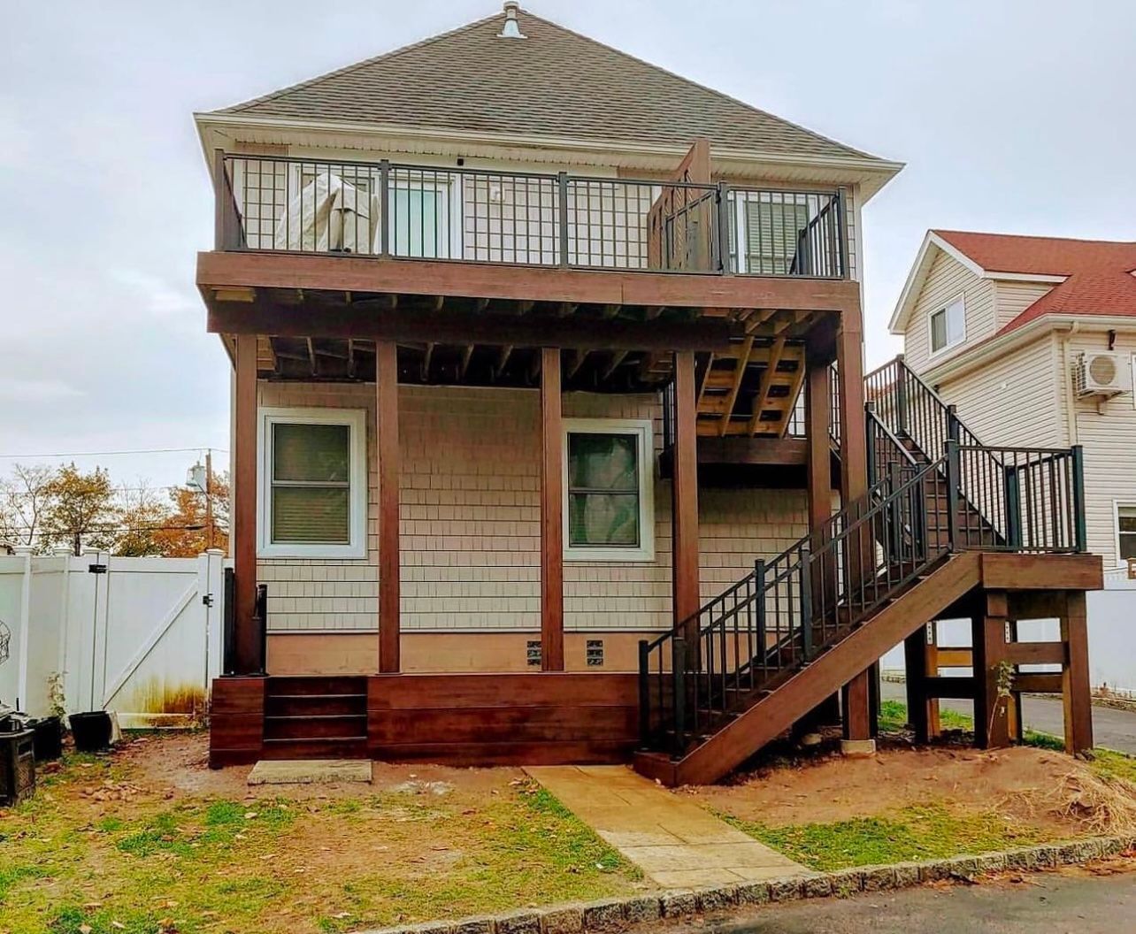 Two-story house with brown decks and stairs. Tan siding, brown railing, gray roof, and a cloudy sky.