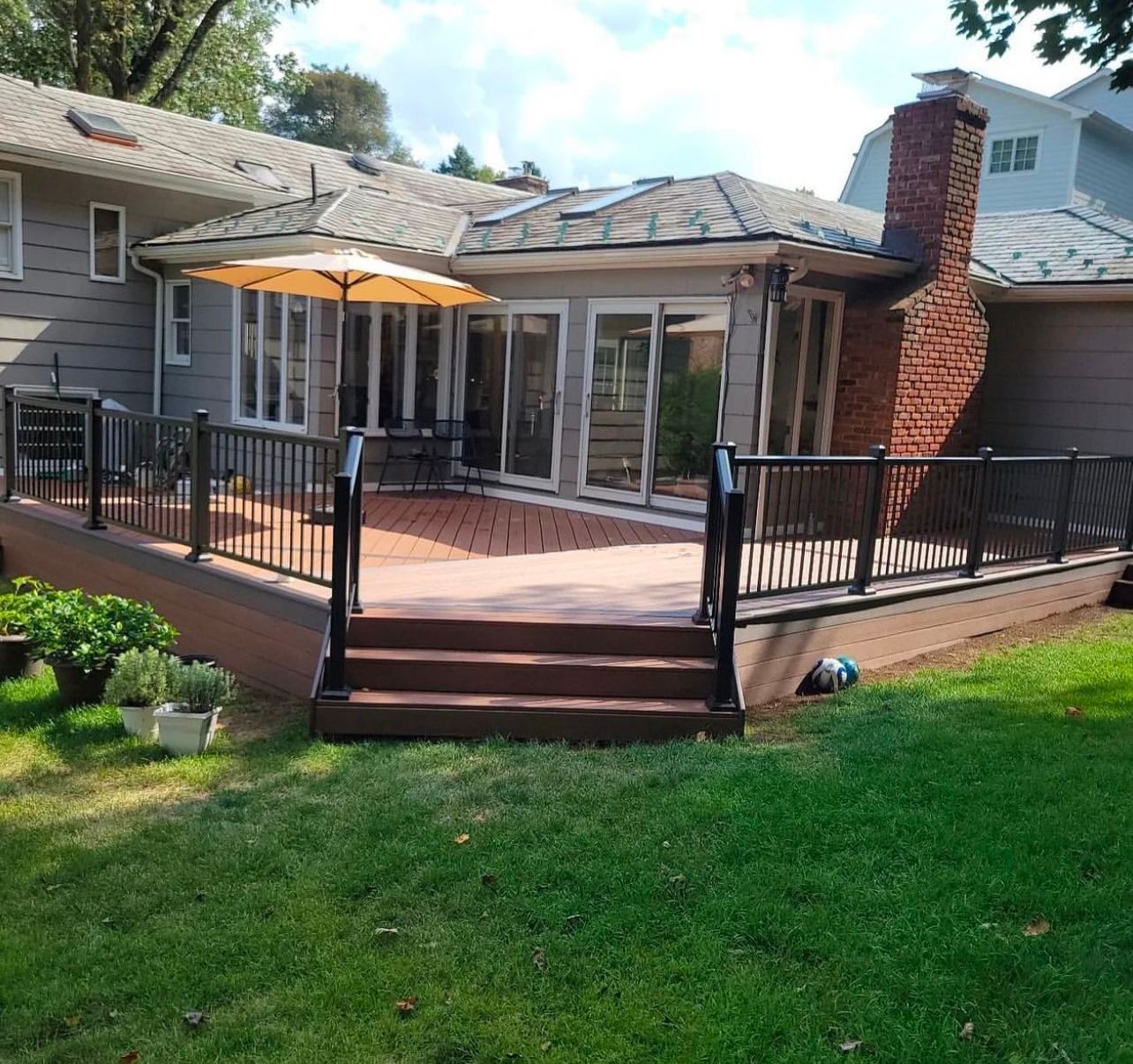 Backyard deck with a brown wooden floor, black railing, and an umbrella.