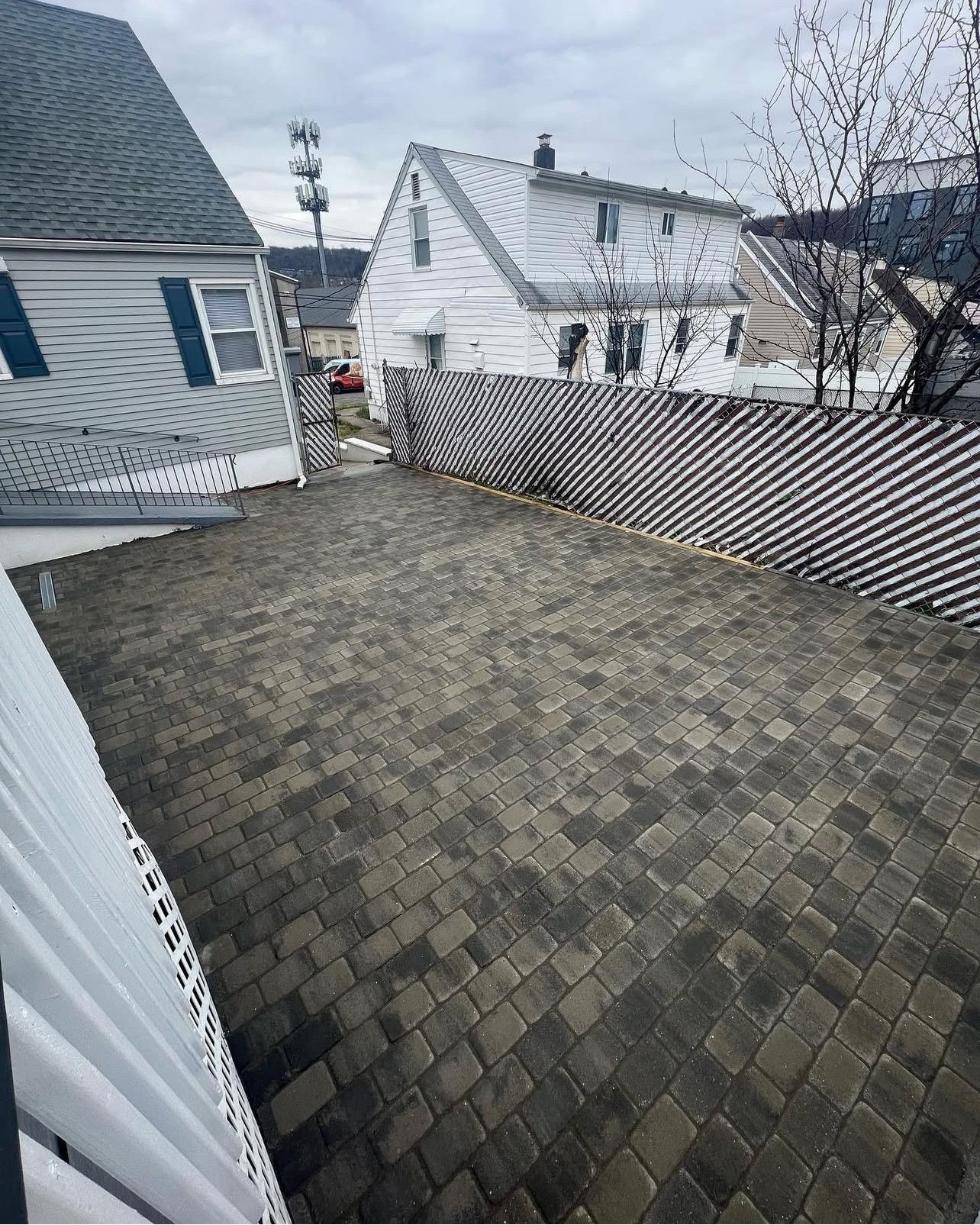 Brick-paved backyard enclosed by a fence. White house and cloudy sky in the background.