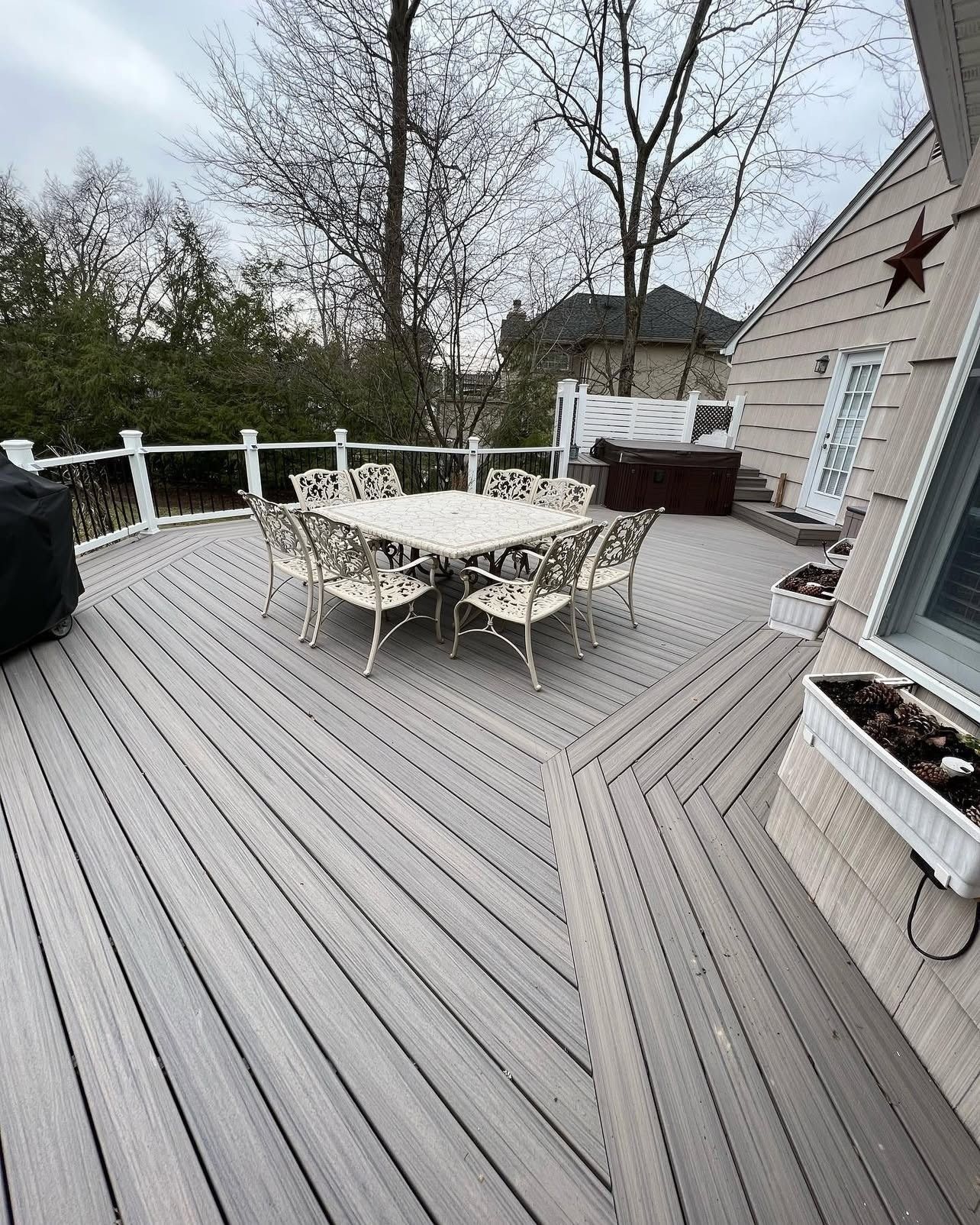 Gray composite deck with dining set, overlooking a backyard, with trees.